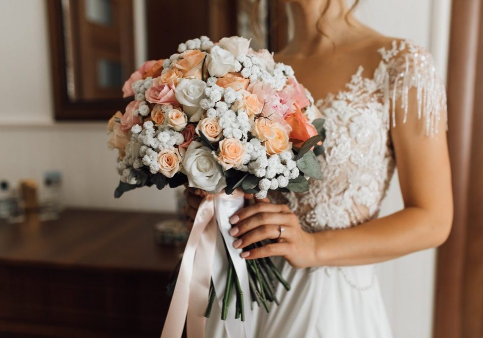 Bride holds the lush bouquet with delicate flowers colors